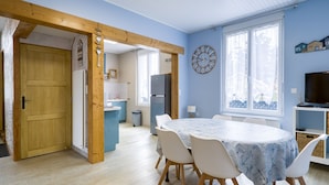 A room with a dining table, chairs, a clock, a television, and a window with a view. - Family Home with Garden near Beach in Châtelaillon – Sleeps 6 (Châtelaillon-Plage)