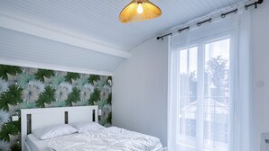 A bedroom with a bed, a window with curtains, a ceiling light, and a wall with a leaf pattern. - Family Home with Garden near Beach in Châtelaillon – Sleeps 6 (Châtelaillon-Plage)