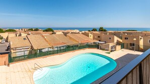 Piscina no terraço com vista para o mar e edifícios com telhados de terracota.