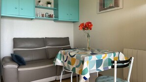 Sala de estar com sofá, mesa com toalha estampada, vaso com flores e armários verde-água.