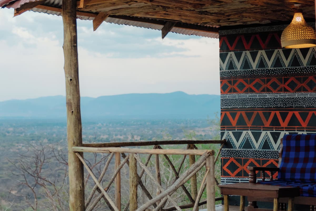 Una estructura rústica de madera con techo de lámina corrugada, pared con diseño y vista a montañas distantes.