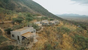 A remote, rustic accommodation with multiple rooms, each featuring a wooden deck and a view of the surrounding hills and sparse vegetation. - RUAHA HILLTOP LODGE (Idodi)