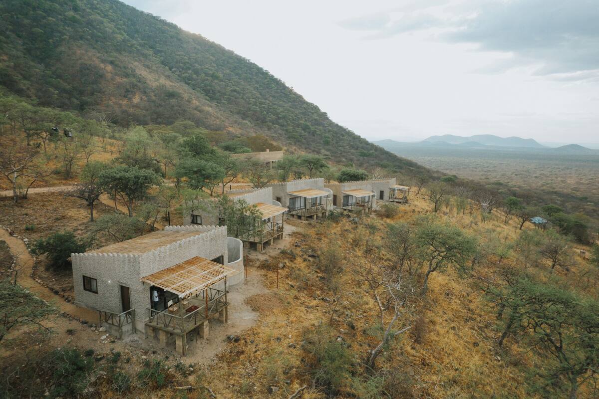 Un alojamiento rústico y aislado, con varias habitaciones, cada una con una terraza de madera y vistas a las colinas circundantes y vegetación escasa.