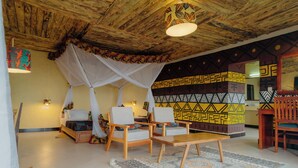 A room with a bed, two chairs, a table, a patterned rug, and a ceiling with wooden beams. - RUAHA HILLTOP LODGE (Idodi)