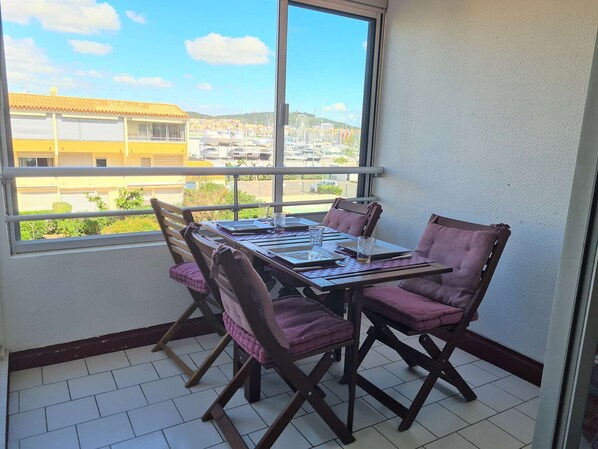 A balcony with a table and chairs, a view of buildings and a clear sky.