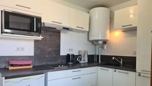 A modern kitchen with white cabinets, a built-in microwave, a coffee maker, and a water heater. - Modern 4-person apartment with pool and parking in Cap d'Agde (Cap d'Agde)