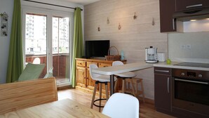 A compact kitchen with a dining area, wooden cabinets, a coffee maker, and a TV.