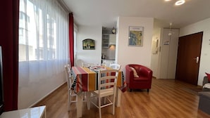 A dining area with a wooden table and chairs, a red armchair, and a kitchen in the background. - T2 Apartment with Parking near La Rochelle Old Port (La Rochelle)