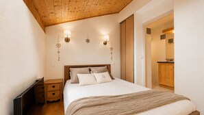 A bedroom with a wooden ceiling, a bed with a white comforter, two bedside tables, and a nightstand. - 3-bedroom duplex at the foot of the slopes with pool and parking (Flumet)