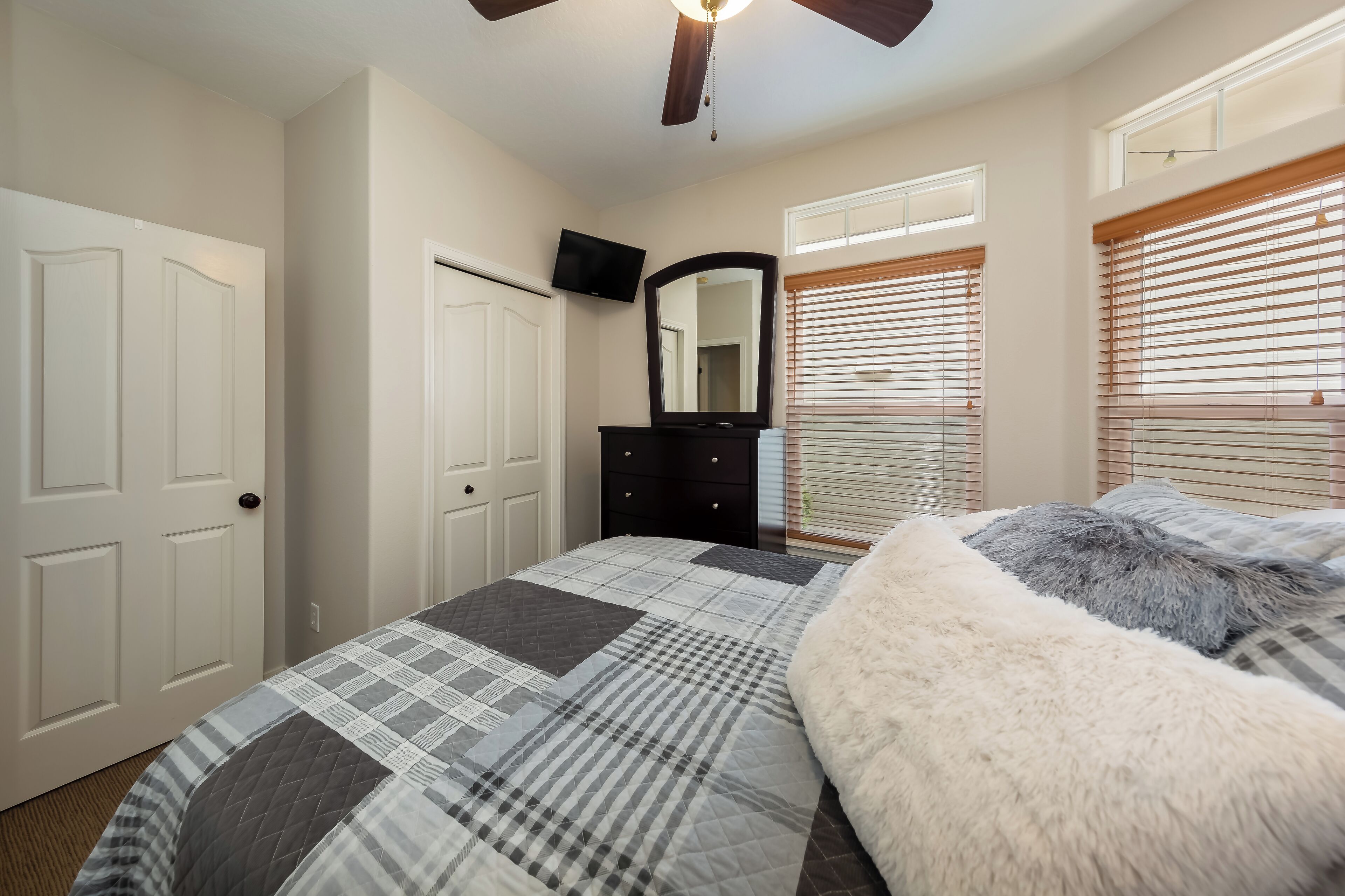 A bedroom with a bed, a dresser, a mirror, a TV, and a ceiling fan.