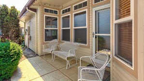 Eine überdachte Terrasse mit Sitzgelegenheit, großen Fenstern und einem kleinen Garten.