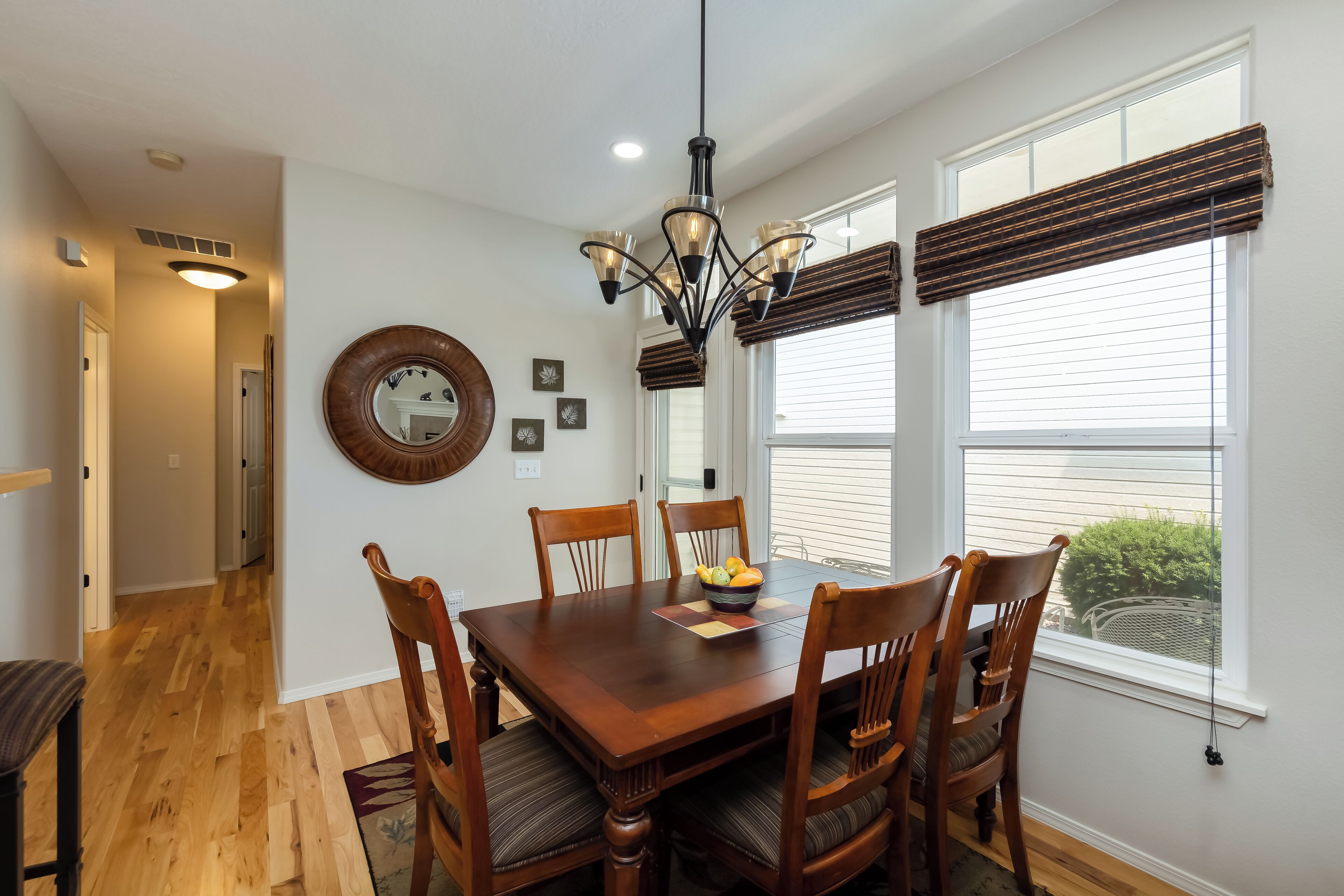 A dining area with a wooden table, chairs, a chandelier, and a window with blinds.