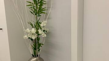 A metallic vase with white flowers and green leaves against a white wall.