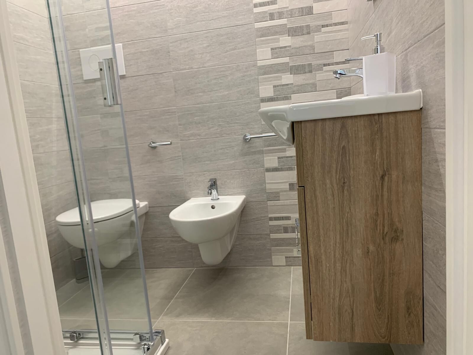 A modern bathroom with a glass shower enclosure, a bidet, and a wooden vanity with a sink.