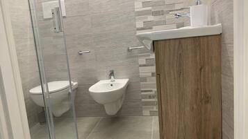 A modern bathroom with a glass shower enclosure, a bidet, and a wooden vanity with a sink.