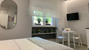Ein modernes Schlafzimmer mit Bett, Schreibtisch, Stühlen, Fernseher und einem Fenster mit Pflanzen.