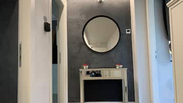 A hallway with a round mirror on the wall, a console table with decorative items, and a door leading to another room.