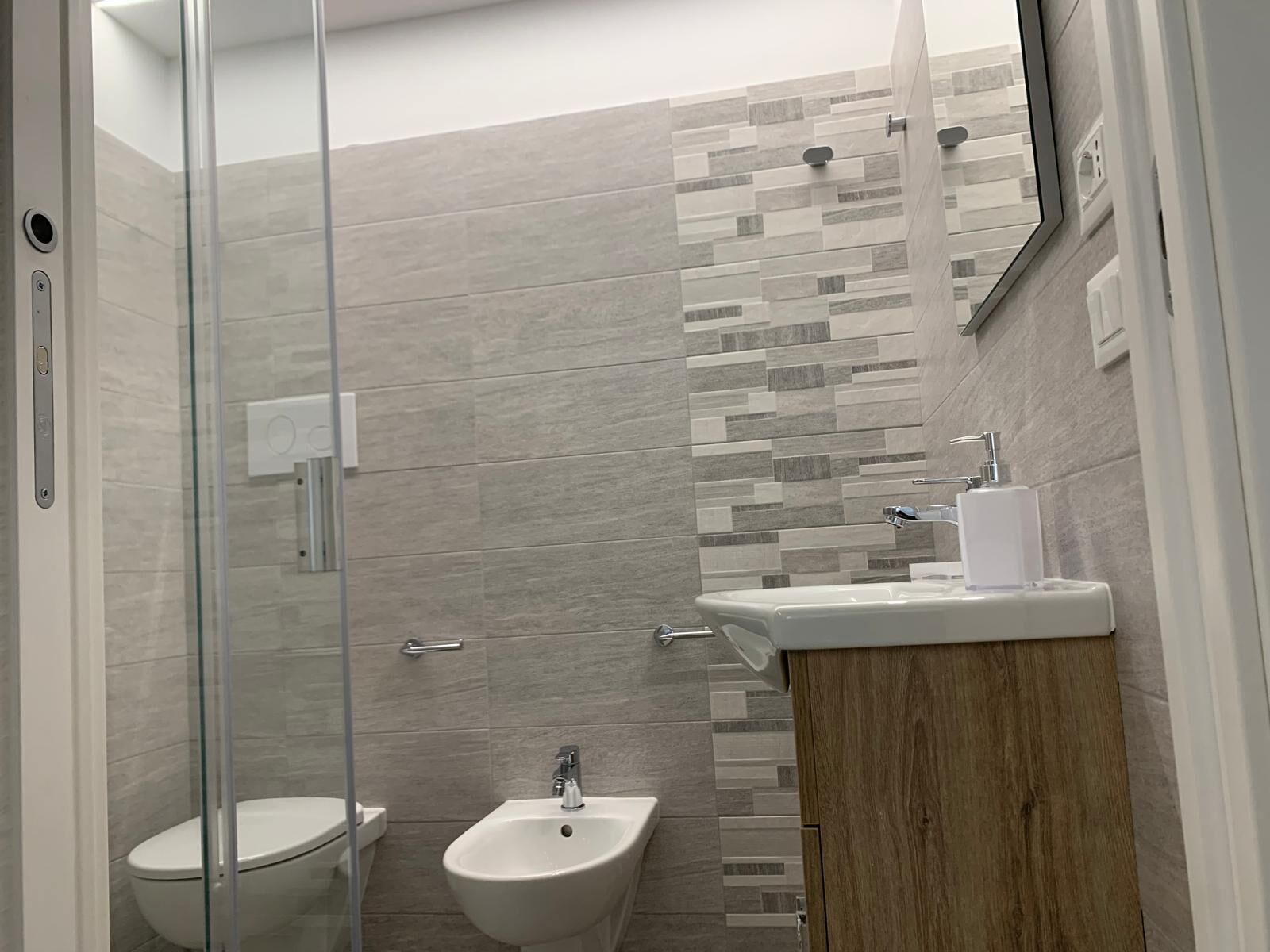 Une salle de bain moderne dotée d’une douche à parois de verre, d’un bidet, de toilettes et d’un lavabo avec un meuble-vasque en bois.