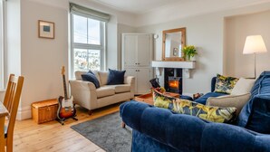 A living room with a sofa, a chair, a guitar, a fireplace, and a view of the outside. - 2 Bed in Brixham (oc-m28892) (Brixham)