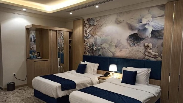 Quarto de hotel com duas camas, um grande mural floral na parede e um guarda-roupa.
