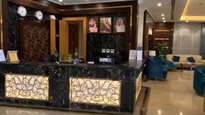 Uma área de recepção de hotel com um balcão de mármore, um espaço de estar com sofás e uma parede decorada com quadros.