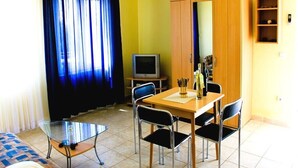 A room with a dining table, chairs, a television, a wardrobe, and a window with curtains. - Niko (Okrug)