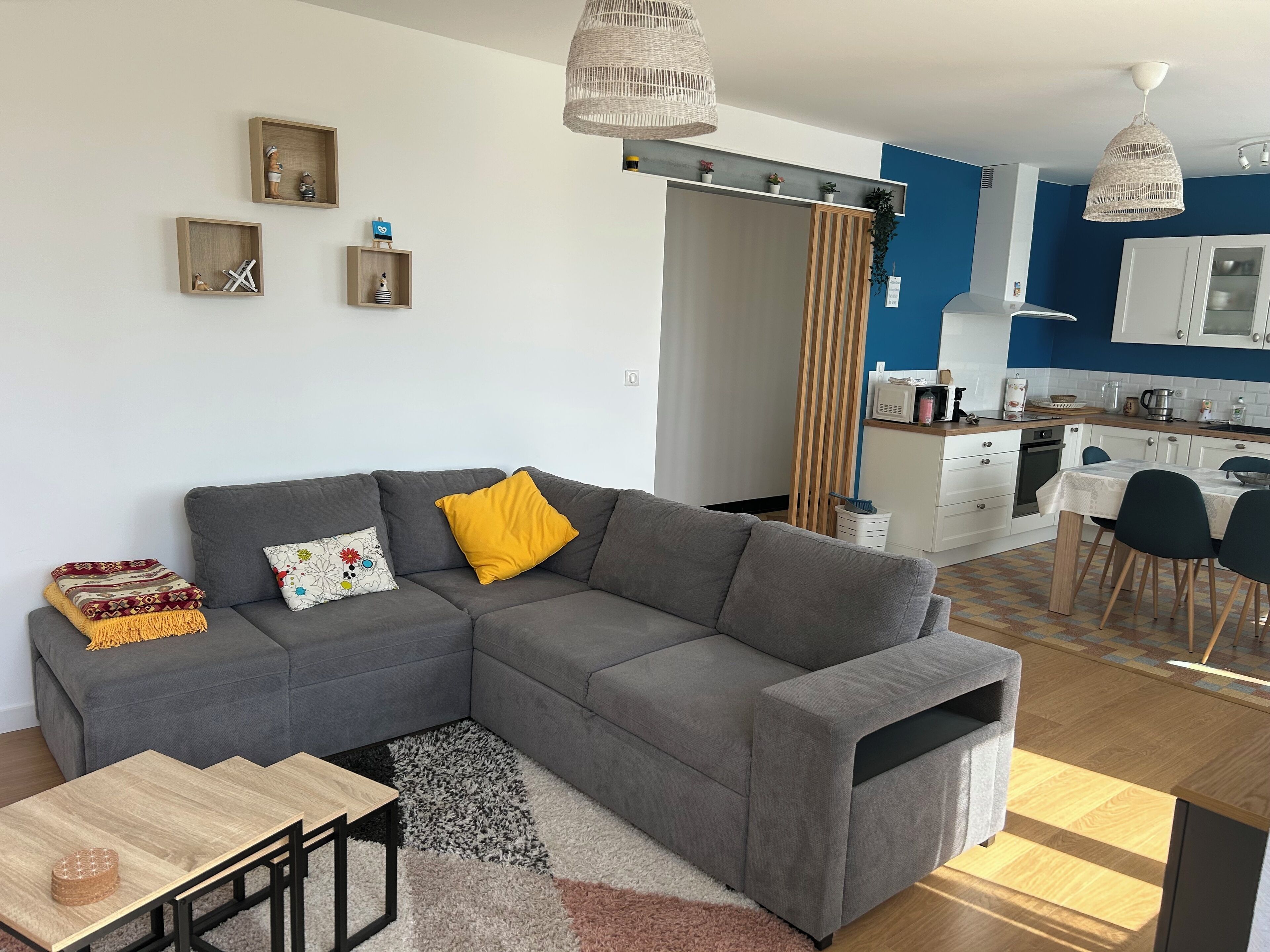 A modern living room with a grey sectional sofa, a small wooden table, and a kitchen in the background.