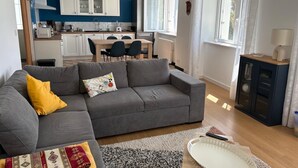 A modern living room with a grey sofa, a patterned rug, and a dining area with a table and chairs. - Maison Pour 6 Personnes, 150 m de la Mer, 4mn à Pied du Port de Pors Poulhan (Plozévet)