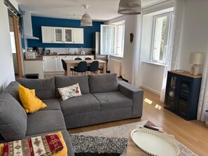 A modern living room with a grey sofa, a patterned rug, and a dining area with a table and chairs.