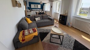 A modern living room with a grey sofa, a coffee table, and a kitchen in the background. - Maison Pour 6 Personnes, 150 m de la Mer, 4mn à Pied du Port de Pors Poulhan (Plozévet)