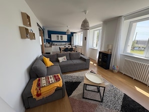 Ein modernes Wohnzimmer mit grauem Sofa, einem Couchtisch und einer Küche im Hintergrund.