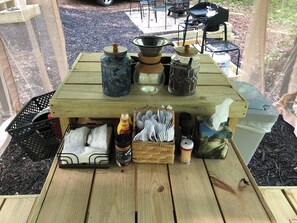 Una mesa de madera con diferentes objetos y utensilios de cocina, como una cafetera, frascos y una cesta de servilletas.