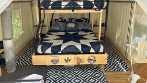 Una cama nido con colcha acolchada, cabecera de madera con la palabra "ENJOY" y un logotipo en el pie de cama.