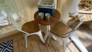 Una terraza de madera con una pequeña mesa redonda, dos sillas blancas y un enfriador azul con tapa blanca.
