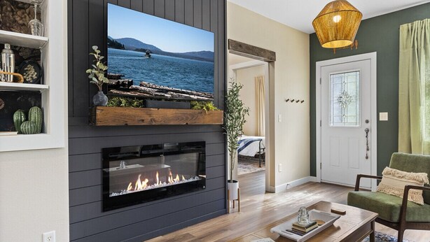 Uma sala de estar moderna com lareira, televisão na parede e vista para um lago.