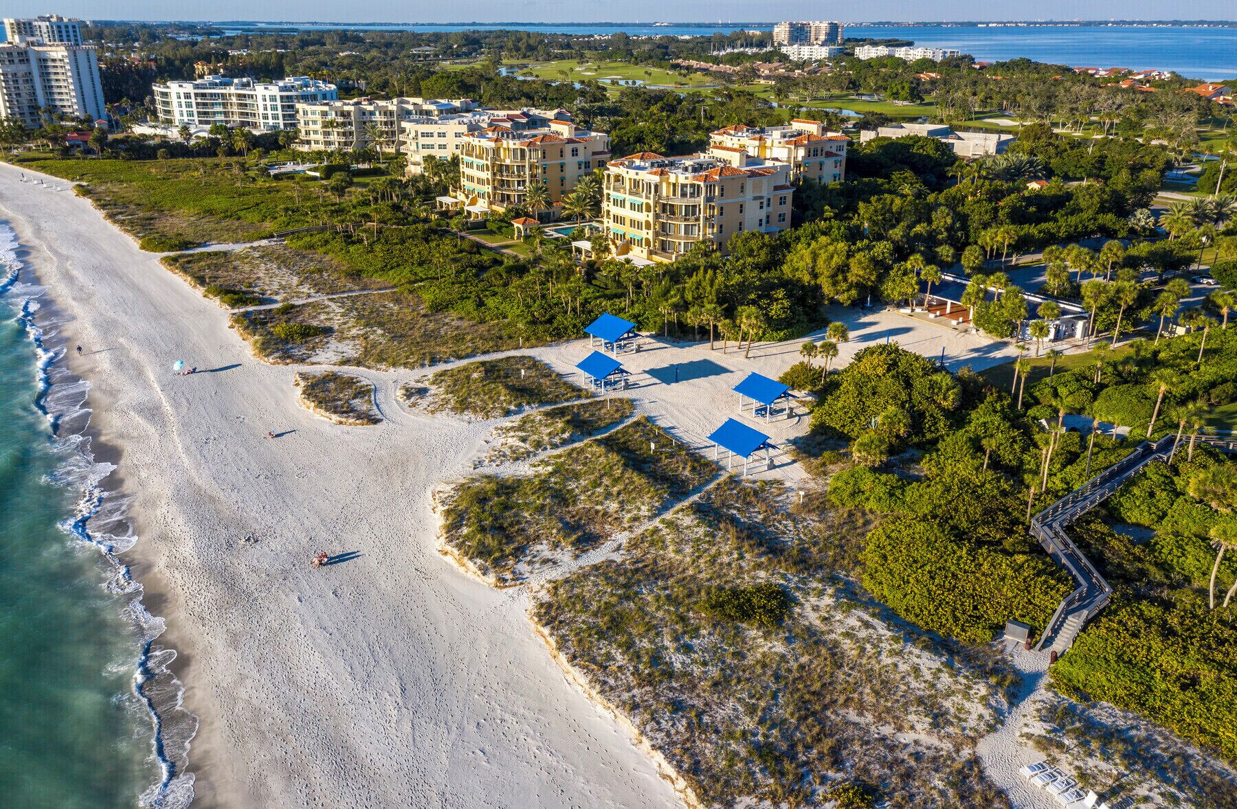 Vista aérea de un resort costero con villas frente a la playa, una playa de arena y un campo de golf.