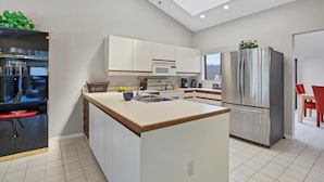 Une cuisine moderne avec des meubles blancs, un îlot central, des appareils en acier inoxydable et un coin repas avec des chaises rouges.