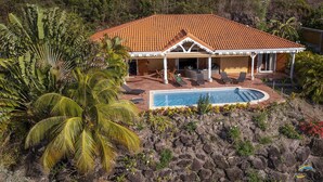 Una casa con piscina rodeada de exuberante vegetación tropical y paisaje rocoso.