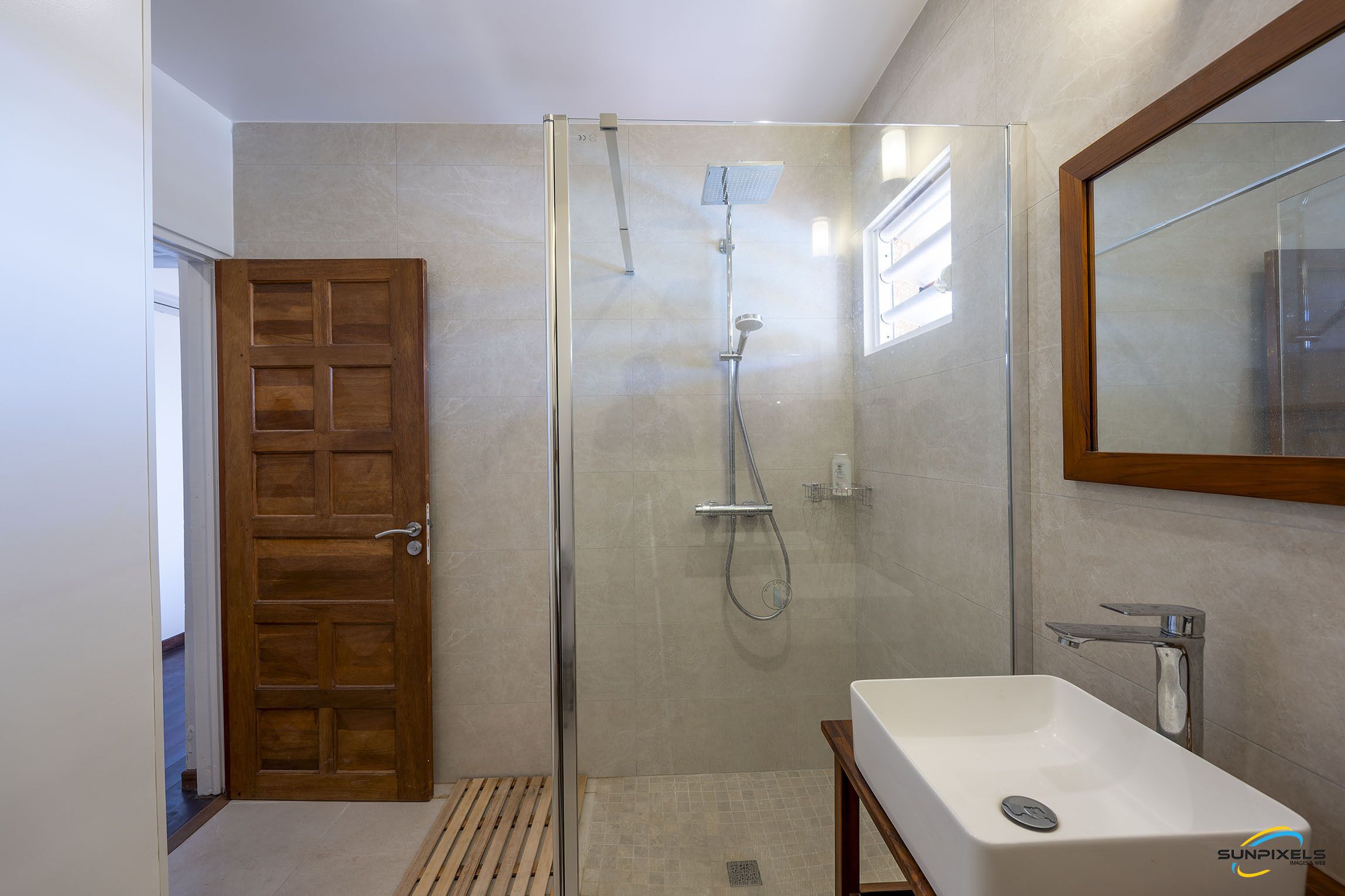 Une salle de bain moderne avec une douche à parois de verre, une porte en bois et un lavabo blanc.