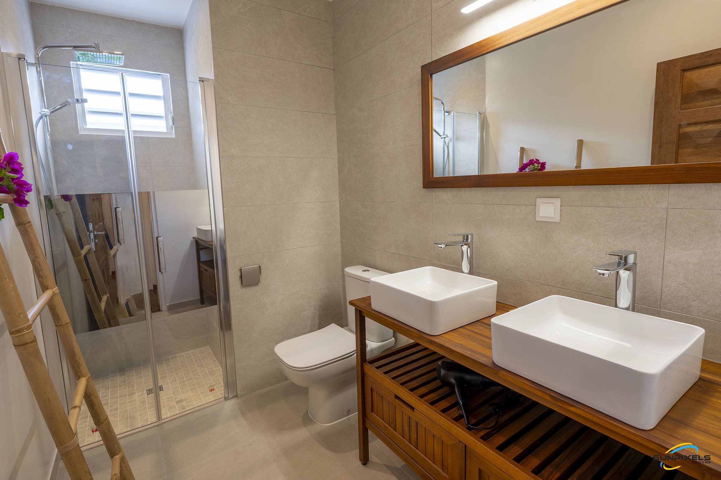 Et moderne badeværelse med en glasbrusekabine, toilet og to vaske på et træbord.