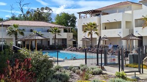 A pool area with lounge chairs and umbrellas, surrounded by a fence.