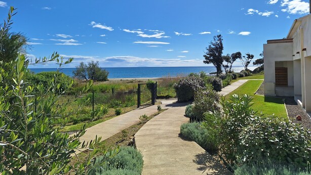 A pathway leading to a beach with a clear view of the ocean and a modern building with a garden.