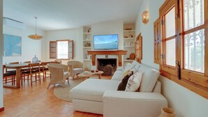 Una sala de estar con sofá, televisor, chimenea, comedor y ventanas amplias.