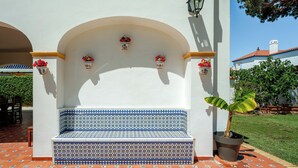 Pared blanca con un banco de diseño azulado, plantas en macetas y una lámpara.