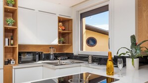 A modern kitchen with white cabinets, a built-in stove, and a window with a view of a building. - De Vivo Realty - Regina Vittoria Relais EcoSmart Luxury Home SPA (Vico Equense)