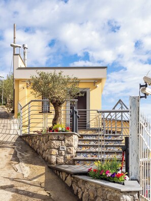 Un edificio con una escalera de piedra, barandillas metálicas y macetas de flores coloridas.