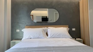 Un letto rifatto con lenzuola bianche, uno specchio rotondo a parete e una testiera in legno.