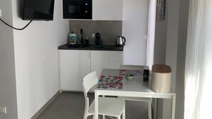 Una cucina compatta con forno a microonde, macchina del caffè e bollitore. C'è un tavolo con tovaglietta e una sedia.