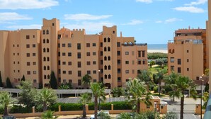 Een hoog hotel met meerdere balkons, uitzicht op het strand en palmbomen op de voorgrond.
