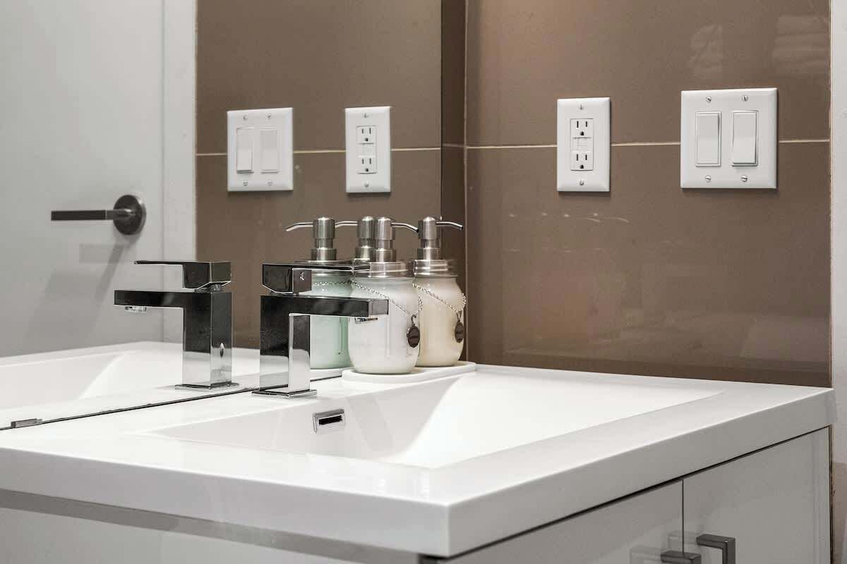 Ein modernes Badezimmer mit einem weißen Waschbecken, einem Chromarmaturen und zwei Wandleuchten.